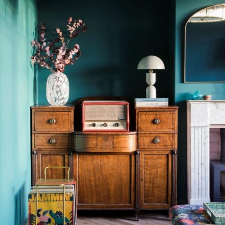 chyby v barvách obývacího pokoje, obývací pokoj s modrozelenými stěnami, vintage skříň, retro motiv, krb, zrcadlo, vintage rádio, vázy, stolní lampa