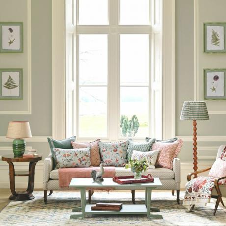 salon z kremową sofą z różowymi i niebieskimi poduszkami oraz standardową lampą
