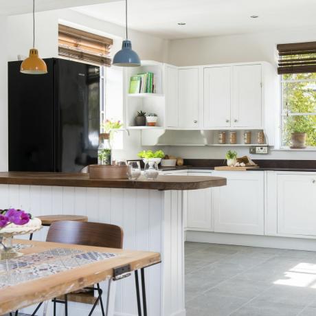 Bílá otevřená kuchyně s pracovními deskami z tmavého dřeva a šedou podlahou