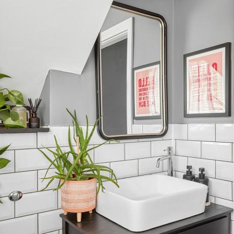Malá toaleta s šedými stěnami, dlaždicemi metra, zrcadlem a umyvadlem