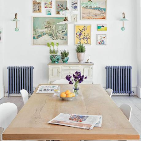 mesa de jantar de madeira com cadeiras brancas na sala de jantar branca brilhante com parede de galeria e radiadores