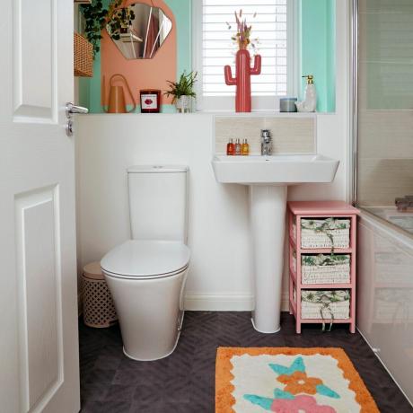 Бяла баня с тоалетна, мивка, вана и декорирана с цветна постелка за баня