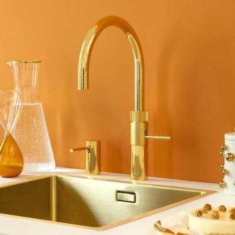 Златен кран за вряща вода върху бял плот в оранжева кухня