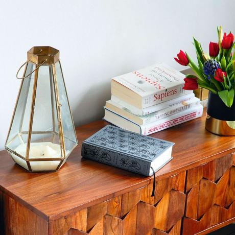 Aparador de madeira com livros, castiçal e vaso de flores em paredes pintadas de cinza claro
