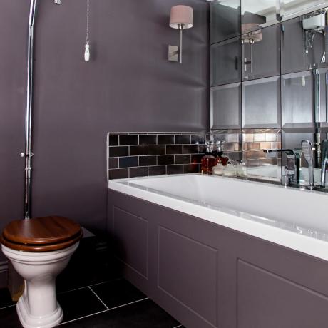 Baño gris pizarra con azulejos espejados detrás de la bañera