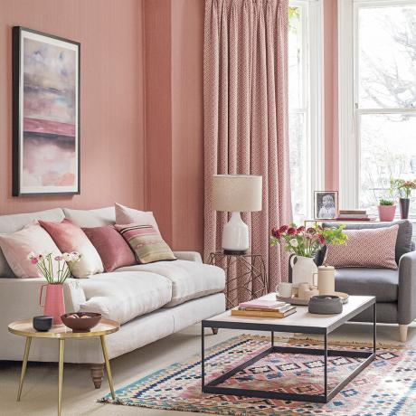 غرفة معيشة باللون الوردي مع أريكة باللون البيج على أرجل وسجادة