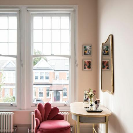 Habitación pintada de luz con grandes ventanas abiertas con persianas blancas, tocador y silla