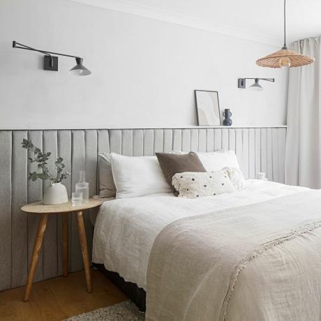 Biała sypialnia z wydłużonym szarym zagłówkiem, nowoczesnymi kinkietami i tkaną lampą sufitową