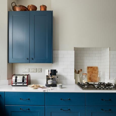 Armários de cozinha azuis com bancada branca e azulejos abaixo das paredes cinza claro