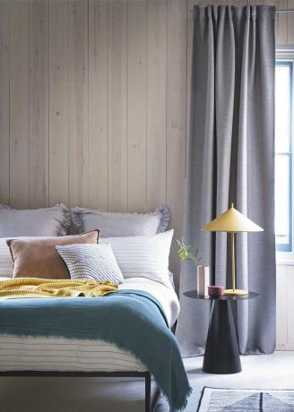 Neutralt sovrum med väggpaneler i blekt trä och grå gardin i full längd