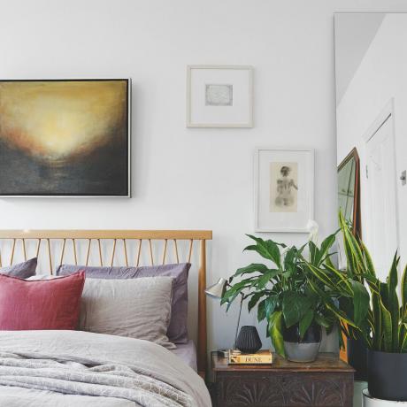 Camera da letto con letto in legno, opere d'arte, piante e specchio a figura intera