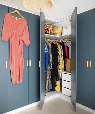 Sumontuotos spintos, nudažytos mėlynai, viduje kabantys drabužiai ir rožinis kombinezonas, pakabintas ant pakabos ant durų