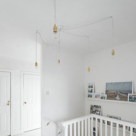 Corredor e escada pintados de branco com luzes pendentes e fotos na parede