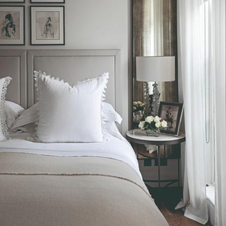 Hvit og grå nøytral seng med sengebord og hvite gardiner
