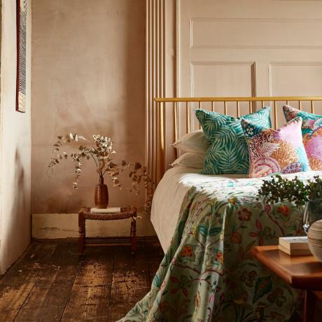Ідеї ​​кольорів для маленької спальні, гіпсові стіни в спальні з дерев’яним ліжком, табуретом із вазою з висушеним евкаліптом, пледом і подушками з яскравим візерунком, творами мистецтва, оригінальними дошками для підлоги