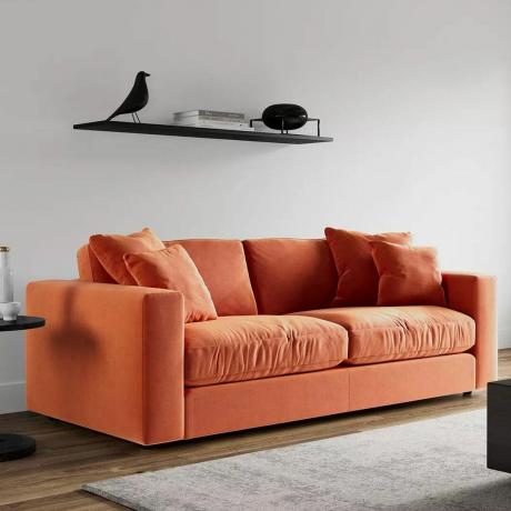Oranžinė sofa su oranžinėmis pagalvėlėmis pilkoje svetainėje