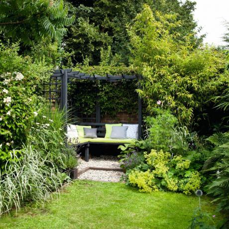 Pěkná zahrada, travnatý trávník, černý rám altánku, lavička, polštáře
