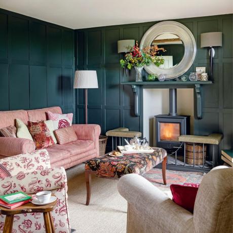 acogedor con paredes con paneles oscuros, sofá rosa y techo claro con lámparas y estufa de leña