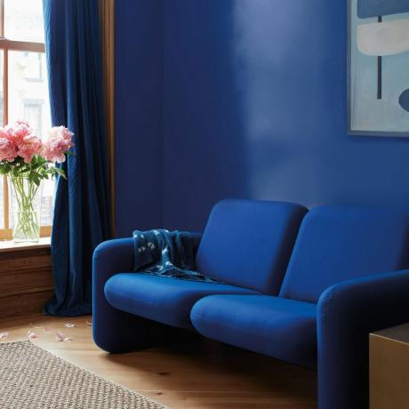 dzīvojamā istaba krāsu krāsas 2023, elektriski zila viesistaba ar spilgti zilu dīvānu, moderns stils, mākslas darbi, peonijas vāzē, zili aizkari, koka grīda, paklājs