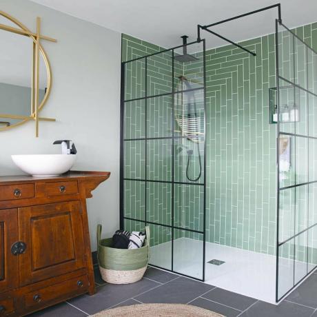 Gri yer karolu banyo, yeşil fayanslı duşakabin, beyaz lavabo ve ahşap banyo çekmeceleri