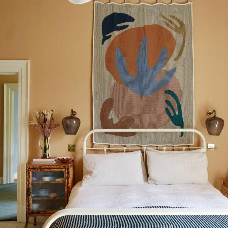Soveværelse med hængende gobelin på væg, mønstret træ sidebord og dekorative møbler