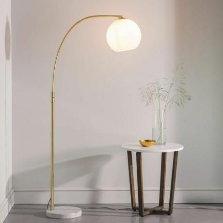Lámpara de pie grande con soporte dorado curvo junto a una pequeña mesa de café