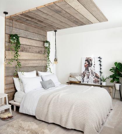 Dormitor alb cu tăblie rustică din scândură de lemn care continuă pe tavan