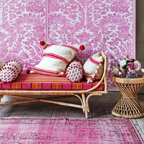 Rožinis ir raudonas dekoras gyvenamajame kambaryje su rotango baldais, plikomis grindų lentomis, pagalvėlėmis ir džiovintomis gėlėmis_JAN-BALDWIN