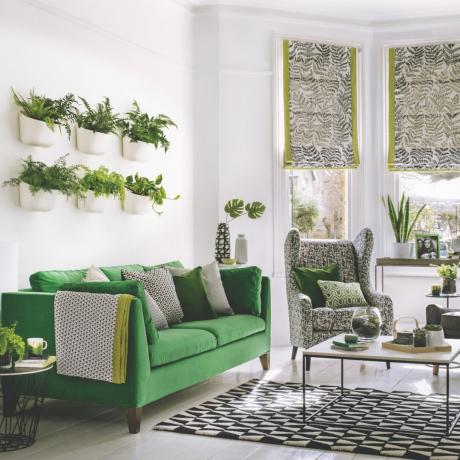 зелено-белая гостиная с зеленым диваном, настенные горшки с папоротником, жалюзи с зеленой окантовкой, черно-белый ковер, черно-белое кресло, зеленые подушки с принтом, журнальный столик