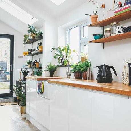 biela kuchyňa s drevenými pracovnými doskami a otvorenými policami vedľa plastového okna
