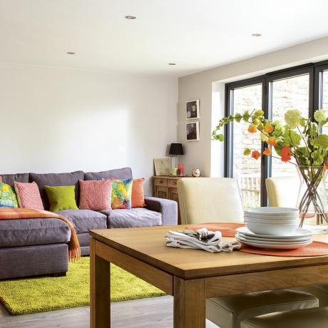 Sala de estar em plano aberto com sofá em forma de L e mesa de jantar de madeira