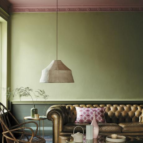 идеи за таван в хола, зелена всекидневна с розов таван, кожен диван с копчета, голяма висяща лампа, стол от ратан, метална масичка за кафе и странична маса