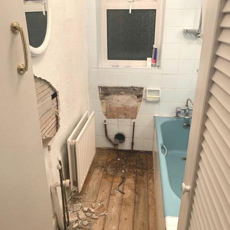kúpeľňa v polovici rekonštrukcie s modrou vaňou a odhalenou drevenou podlahou