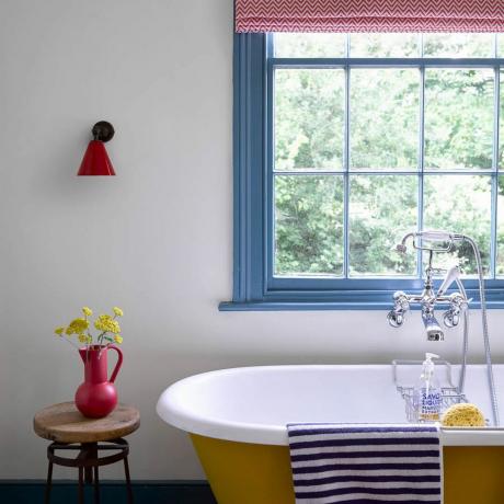 बजट बाथरूम विचार, नीले रंग की खिड़की के फ्रेम के साथ बोल्ड रंगीन बाथरूम, पीला स्नानघर, लाल फूलदान, लाल दीवार की रोशनी, धारीदार नीला तौलिया, लाल ग्राफिक ब्लाइंड