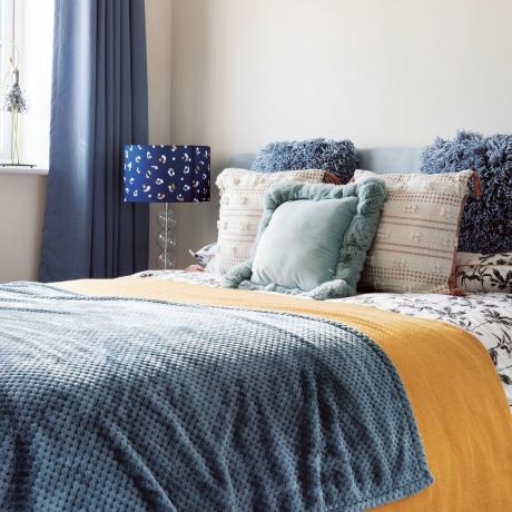 Гостевая спальня с белыми стенами, синими шторами, фактурными подушками, синей декоративной панелью и настольной лампой с анималистическим принтом