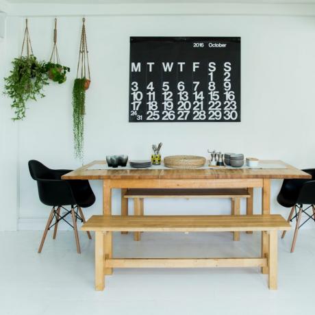 벤치 좌석이 있는 흰색 식당, Eames 스타일 의자 2개, 달력 벽걸이, 화초