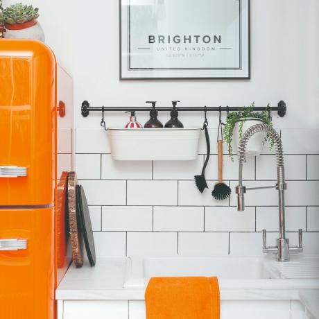 オレンジ色の冷蔵庫とティータオルを備えた白いタイル張りのキッチン