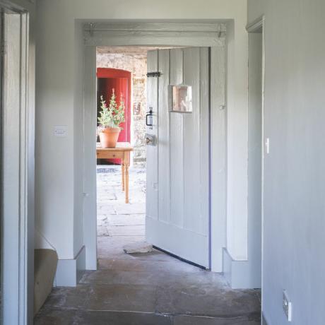 幅木カラーのアイデア、グレーと白の農家スタイルの廊下、石の旗、別の部屋への出入り口、グレーの幅木と木工品