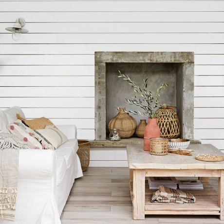 Білий диван і дерев'яний журнальний столик з вазами перед стіною з білими панелями