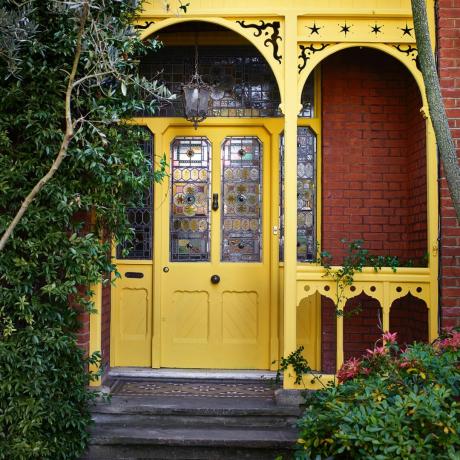kesalahan ide warna pintu depan, pintu depan dan teras kuning dengan detail hiasan bergaya Victoria, jendela kaca patri, tangga hingga area ubin