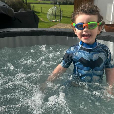 Uma criança usando óculos de proteção e um maiô azul na banheira de hidromassagem Wave Osaka cheia de água azul borbulhante
