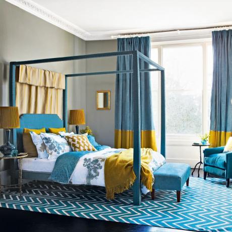 Lova su baldakimu mėlyname miegamajame su dideliu kilimėliu