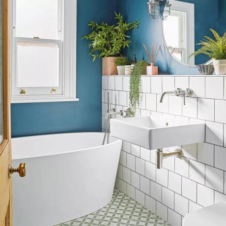 Kylpyhuoneessa siniset seinät, valkoiset laatat ja soikea kylpyamme