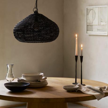 Una mesa de comedor con candelabros de metal negro, una lámpara colgante baja y vajilla.