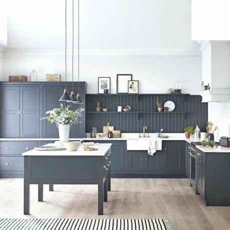 tamsiai mėlynos virtuvės spintelės ir prie baltų sienų ir lubų derančios tamsios sienų dailylentės bei šviesios medienos grindys