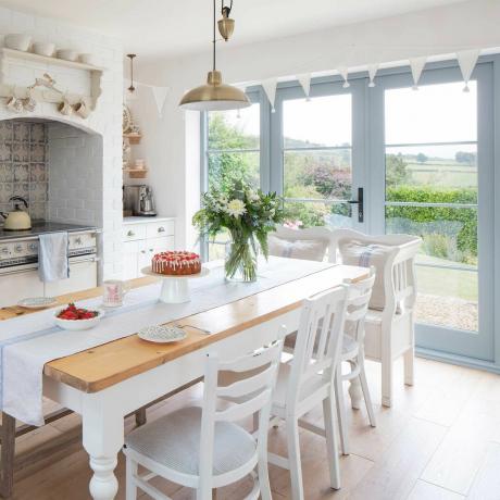 cozinha de casa de campo branca com mesa de fazenda, fogão e portas francesas para o jardim