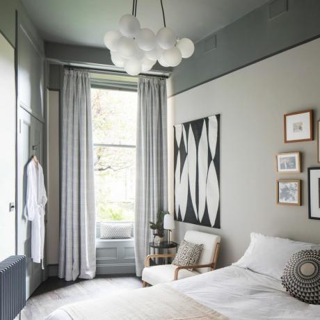 Weiß gestrichenes Schlafzimmer mit großen Fenstern, langen weißen Vorhängen und Bett