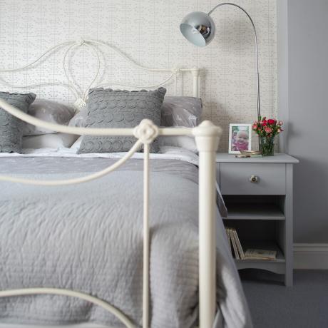 크림색 금속 침대와 부드러운 무늬의 벽지가 있는 회색 침실 
