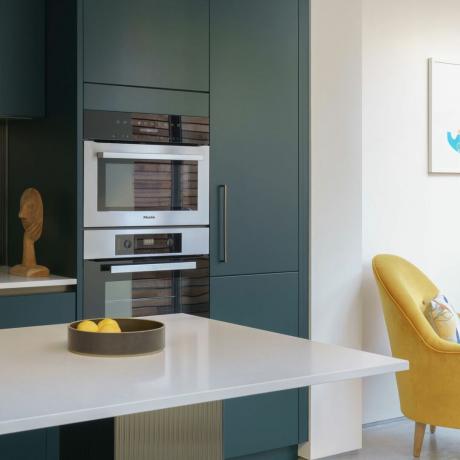 moderne groene keuken met ingebouwde ovens en een gele fauteuil