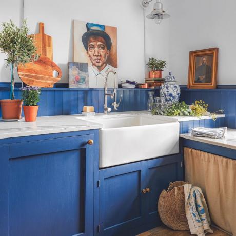 Spilgti zila virtuve ar kratītāju skapjiem, atvērtiem plauktiem un Belfāstas izlietni.